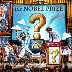 Un scientifique en blouse blanche reçoit un trophée humoristique en forme de point d’interrogation lors de la cérémonie des prix Ig Nobel, sous les rires du public.